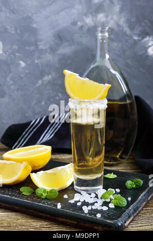 Mexican Gold Tequila nel colpo di vetro con limone e sale di mare sul tavolo scuro. In stile retrò, vintage. Foto Stock