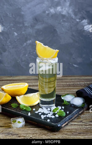 Mexican Gold Tequila nel colpo di vetro con limone e sale di mare sul tavolo scuro. In stile retrò, vintage. Foto Stock