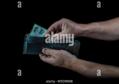 Le mani di uomo prendendo una cinquecento peso argentino bill da un portafoglio, su sfondo nero Foto Stock