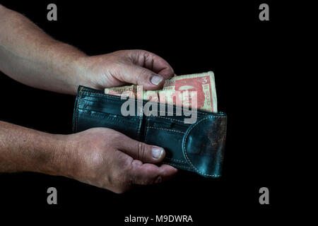 Le mani di uomo prendendo un tre peso cubano bill da un portafoglio, su sfondo nero Foto Stock
