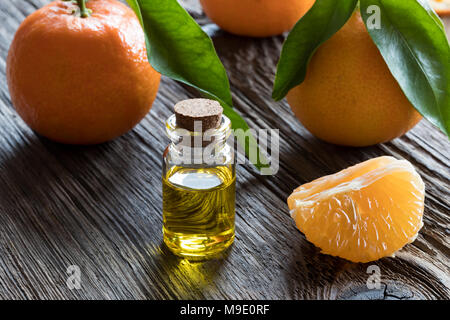 Una bottiglia di mandarino olio essenziale su legno antico, con freschi Mandarini in background Foto Stock