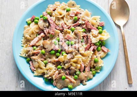 Cremosa di prosciutto e funghi farfalle. La pasta alla carbonara con prosciutto e funghi, piselli in salsa di formaggio cremosa. Foto Stock