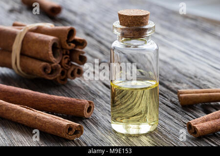 Una bottiglia trasparente di cannella olio essenziale con bastoncini di cannella su uno sfondo di legno Foto Stock