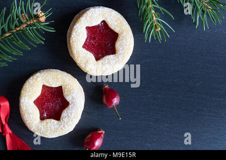 Scuro dello sfondo di Natale con due Linzer biscotti di Natale, essiccato, rosa canina e rami di abete rosso Foto Stock