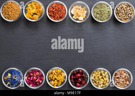 Mix di erbe su sfondo scuro con copia spazio: fieno greco, calendula, sandalo, incenso resina, Equiseto, cardo, Fiordaliso, petali di rose Foto Stock