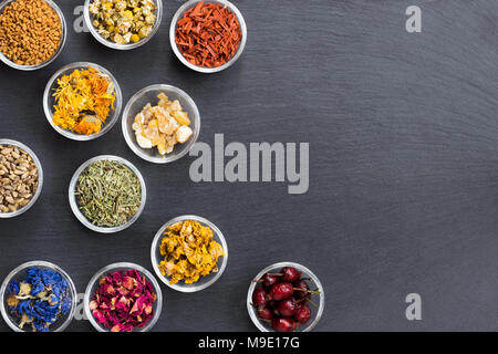 Mix di erbe su sfondo scuro con copia spazio: fieno greco, calendula, sandalo, incenso resina, Equiseto, cardo, Fiordaliso, petali di rose Foto Stock