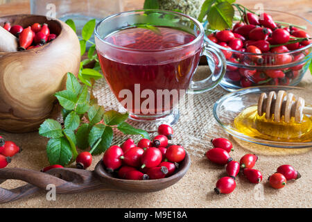 Fresche, rosa canina, rose hip tea e miele su una tavola di legno Foto Stock