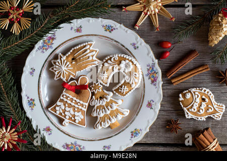 Vista superiore del Natale gingerbread cookie su una piastra su un tavolo in legno con ornamenti di paglia, anice stellato, cannella, rosa canina e rami di abete rosso in t Foto Stock