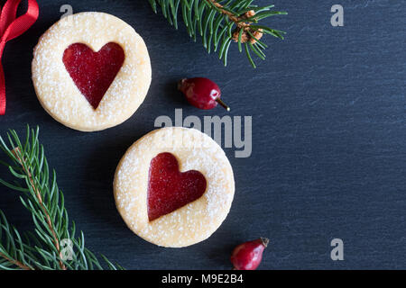 Sfondo di natale con due Linzer biscotti di Natale con cuore forme, essiccato, rosa canina e rami di abete rosso Foto Stock