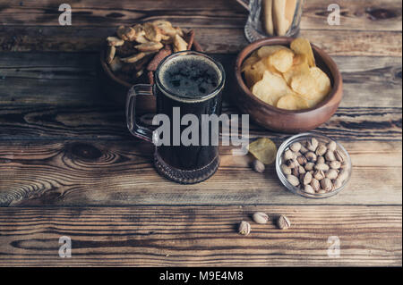 Birra scura in una tazza alta. Spuntini per la birra su di un tavolo di legno. Chip, crostini, grissini Foto Stock