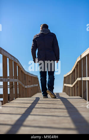 Vista posteriore di un uomo a piedi sulla passerella di legno. Foto Stock