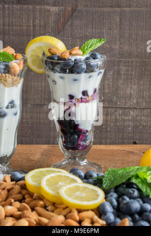 Trattare sano - lo yogurt greco in un dessert fantasia vetro - parfait con mirtilli freschi, mandorle tritate, granola, una spremuta di limone e rametto di menta Foto Stock