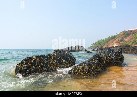 Pietre fuori del mare blu turchese sullo sfondo la costa rocciosa. Goa in India. Foto Stock