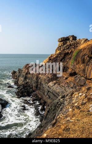 La ripida costa rocciosa con il blu del mare e le onde che si infrangono sulle rocce. Gokarna India Foto Stock