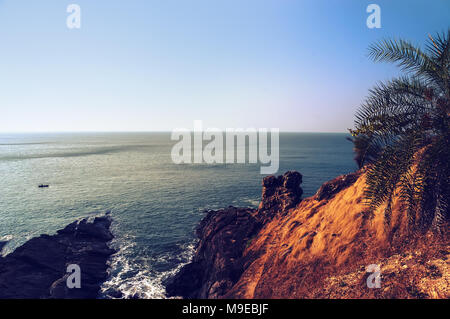 La ripida costa rocciosa con il blu del mare e le onde che si infrangono sulle rocce. Gokarna India Foto Stock