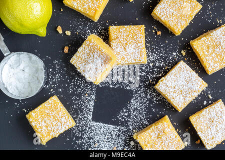 Piazze di limone sulla superficie nera con limone e zucchero a velo - vista superiore foto Foto Stock