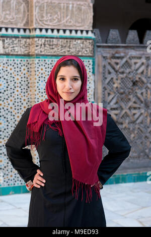 Donna musulmana in posa di abbigliamento tradizionale con red hijab e abito nero nella parte anteriore del tradizionale decorata arabesque parete Foto Stock