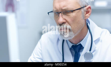 Close-up verticale di un pelo bianco medico che lavorano su Personal Computer. Il suo ufficio è luminoso e luce. Foto Stock