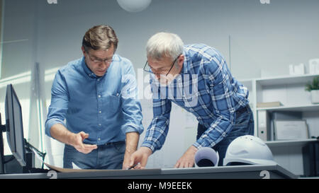 Due tecnici senior lavorare con programmi e progetti mentre sta in piedi sulla tavola di lavorazione. Essi hanno la discussione sul tema della questione tecnica Foto Stock