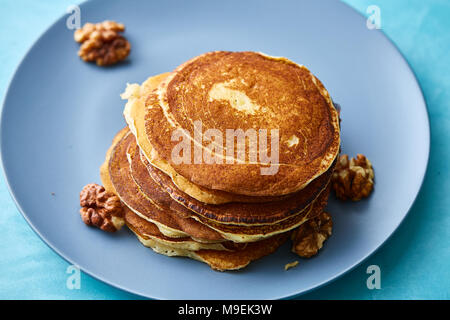 Pila di gustosi pancake fatti in casa con le noci sulla piastra azzurrognolo su sfondo blu, il fuoco selettivo. Una sana deliziosa crepes. Voglia di uno spuntino. Perfetta pa Foto Stock