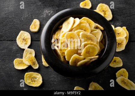 Cumulo di Banane essiccate chips snack nella ciotola nero scuro sul tavolo rustico Foto Stock