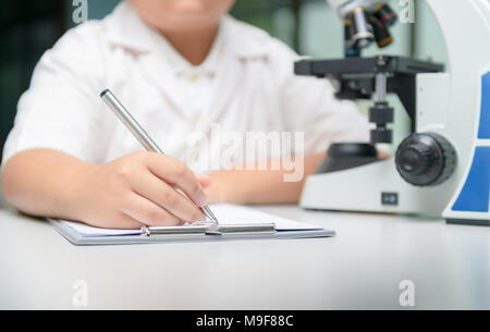 Progetto di ricerca. Piccolo chimico boy scrivendo sui suoi appunti durante il lavoro presso il laboratorio della scuola di scienza e educazione Nozione Foto Stock