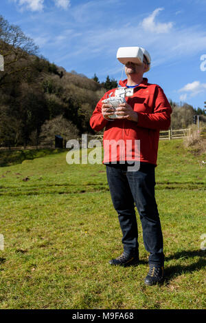 Wye Valley, Monmouthshire, Regno Unito. 25 marzo 2018: l'uomo in escursionismo vestiti, volare un quadcopter drone utilizzando FPV gli occhiali di protezione Foto Stock