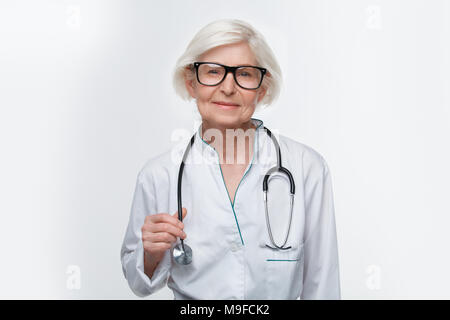Le donne più anziane medico indossando occhiali studio isolato su sfondo bianco tenendo uno stetoscopio cercando fotocamera a sorridere fiducioso Foto Stock