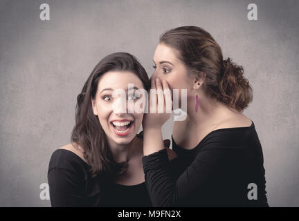 Due vestiti di fantasia attrice ragazze con i capelli lunghi e make up whispering nella parte anteriore del grigio Sfondo urban concept. Foto Stock