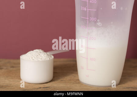 La proteina del siero di latte in polvere bodybuilding sportivi supplemento. Close up di scoop con polvere di vaniglia e shaker su tavola di legno. Colore di sfondo: marrone. Foto Stock