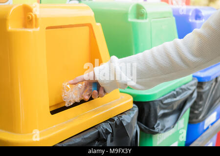 Chiudere la mano a buttare via una bottiglia di plastica in pubblico bin Foto Stock