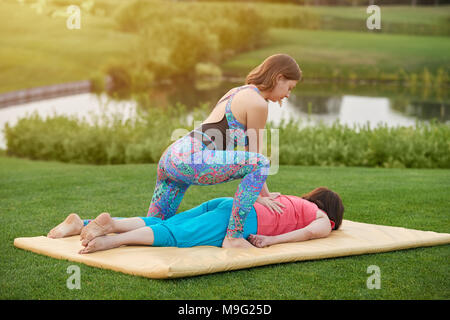 Donna facendo massaggio della schiena per donna. Adorabili e belle donne. Giacente sul tappetino sull'erba. Foto Stock