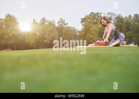 Esercizi di yoga in estate. Piano distante di due donne facendo il massaggio thai sull'erba. Foto Stock