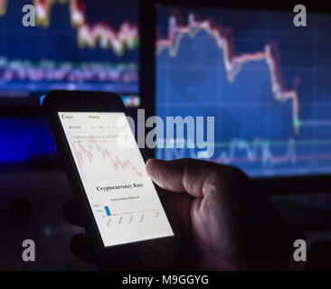 Valuta Crypto day trader azienda telefono mobile guardando i grafici davanti allo schermo del computer nel buio, Vienna Austria 25-3-2018 Foto Stock