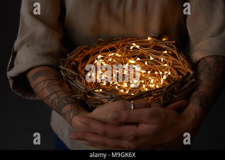 Nido con le luci di Natale nelle mani della donna su sfondo nero Foto Stock