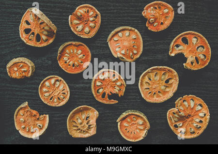 Le erbe aromatiche essiccate e secchi Frutta bael, vista dall'alto di bael a secco sul pavimento di legno, fette di frutta bael per rendere il succo di bael sul tavolo scuro. Foto Stock