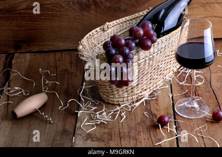 Uve su un cestello per servire il vino con una bottiglia e un wineglass su un rustico sfondo di legno Foto Stock