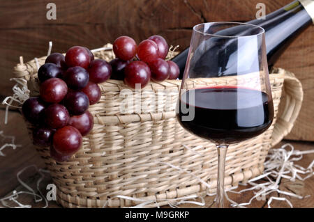 Chiudere su un wineglass nella parte anteriore delle uve su un cestello per servire il vino di bottiglia su un rustico sfondo di legno Foto Stock