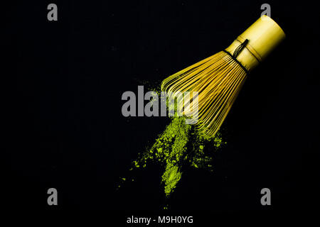 Close up frusta di bambù e il tè verde Matcha polvere su sfondo nero. Foto Stock