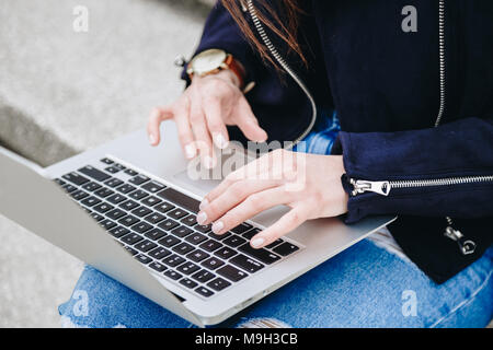 Giovane e attraente fashion blogger a scrivere un nuovo post sul blog sul suo computer portatile. donna attraente con il suo pc all'aperto, indossare un orologio da polso. Foto Stock