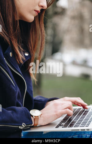 Giovane e attraente fashion blogger a scrivere un nuovo post sul blog sul suo computer portatile. donna attraente con il suo pc all'aperto, indossare un orologio da polso. Foto Stock