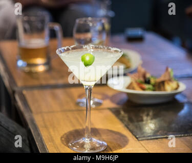 Un drink di margarita si siede su un tavolo nel fuoco. Sullo sfondo sono una varietà di bevande alcoliche, compresa la birra e il vino. Foto Stock