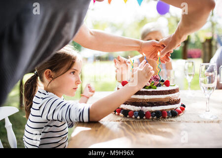 Festa di famiglia al di fuori nel cortile. Grande party in giardino. Festa di compleanno. Piccola ragazza con una torta di compleanno. Foto Stock