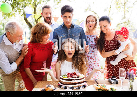 Festa di famiglia al di fuori nel cortile. Grande party in giardino. Festa di compleanno. Una ragazza con una torta di compleanno. Foto Stock