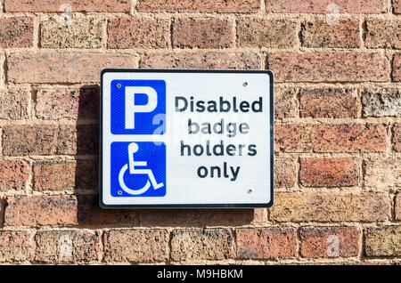 Segno sul muro di mattoni nel parcheggio auto dicendo il parcheggio per disabili titolari di badge solo Foto Stock