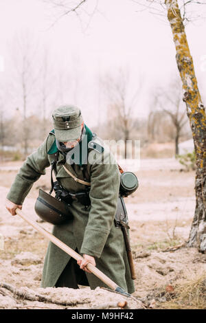 Unidentified ri-enactor vestito come un tedesco Soldato di fanteria della II Guerra Mondiale lo scavo di una trincea in autunno foresta. Foto Stock