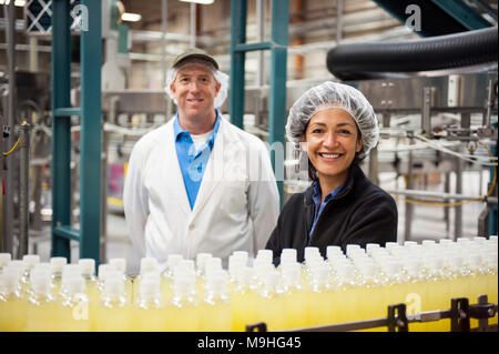 Ritratto di un maschio caucasico e americano africano team femminile dei lavoratori Indossare retine di testa e stare vicino a un nastro trasportatore di aromatizzato al limone acqua ho Foto Stock