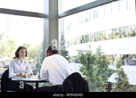 Business donna e uomo in un pranzo informale incontro a una tabella in un aprire l'area della lobby. Foto Stock