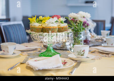 Piastra della deliziosa casa tortini alla vaniglia con glassa di crema di burro e rabboccato con splendidi fiori freschi su un bellissimo set table. Foto Stock