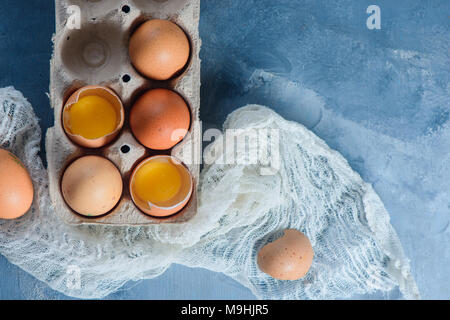 Uova fresche, intere e rotte, in un imballo di carta su un sfondo di calcestruzzo. Gli ingredienti freschi per la Pasqua di cottura. Close-up con spazio di copia Foto Stock